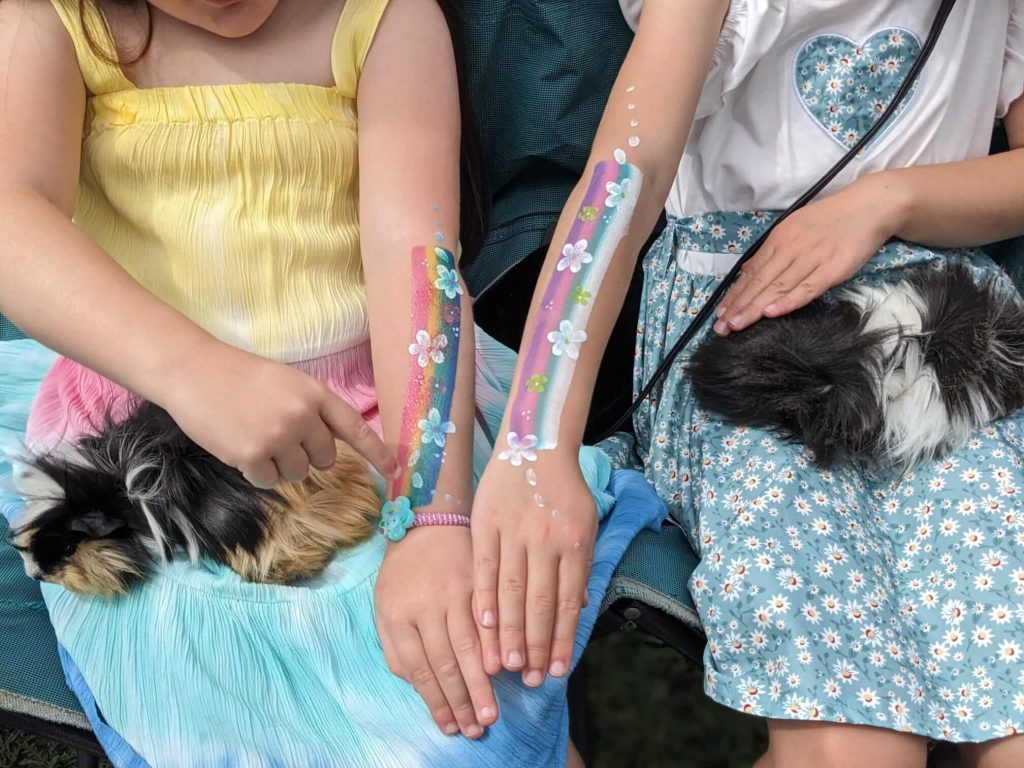 Image of two girls with their arms painted with flowers and rainbows